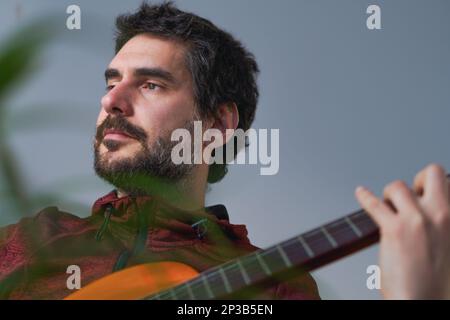 young bearded man playing spanish guitar  blue background with copy space Stock Photo