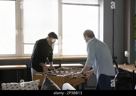Engaged active office colleagues men playing table soccer Stock Photo
