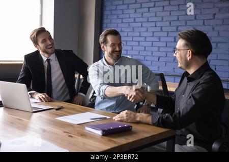 Happy business partner men shaking hands at work office table Stock Photo