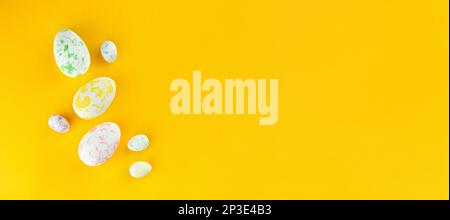 Colored chicken and quail eggs of different colors lie on a yellow background.  Top view, lots of space Stock Photo