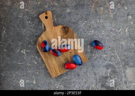 Blue and red dyed eggs lie on a wooden cutting board on an old dark stone table.  Lots of empty space Stock Photo