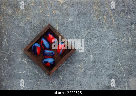Eggs painted blue and red for Easter lie in a wooden box on an old stone background.  Lots of empty space Stock Photo