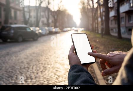 Male person touching screen on mobile phone with finger on city road background. Stock Photo