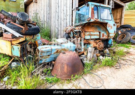 A pile of rusty scrap metal and truck tires in the backyard of a farm in summer Stock Photo