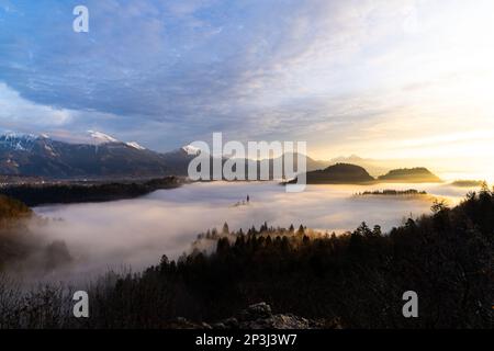 2022 12 30, Bled, Slovenia: Lake Bled covered in fog with Island Bled peaking through and Castle Bled and Julian Alps in the background Stock Photo