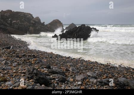 Stormy Atlantic Ocean waves breaking onto the pebble beach and rocks at Praia do Abano Stock Photo
