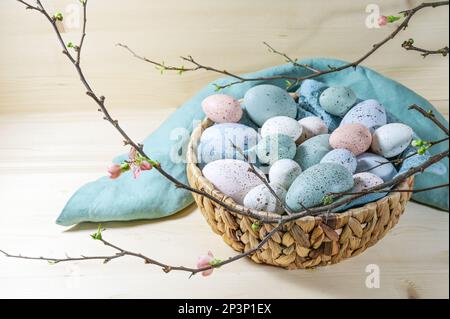 Many pastel colored Easter eggs in a basket and a branch with some flowers on a wooden table, copy space, selected focus, narrow depth of field Stock Photo