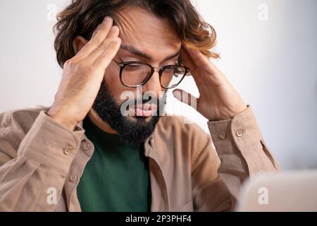 Worried man suffering from headache at work thinking about problems and project deadline. Stock Photo