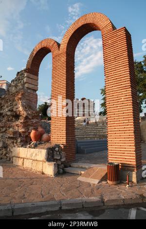 Nessebar, Bulgaria - July 20, 2014: Ruined church and stone arches around the old Nessebar town. Ordinary people walk the street Stock Photo