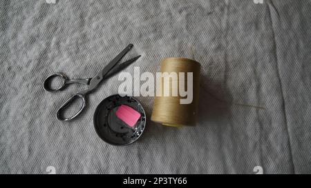 Top of view of sewing materials. Scissors, thread and needle on a fabric background. Stock Photo