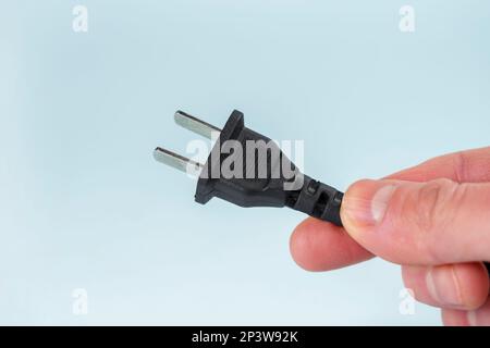 US power plug with cable on a blue background in hand closeup Stock Photo