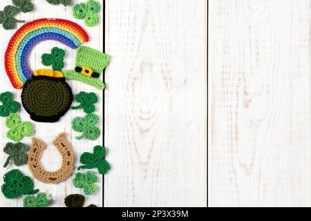 St Patrick's Day concept. Knitted composition of a green hat, a pot of gold, a horseshoe, a rainbow and green shamrocks on a white wooden background. Stock Photo