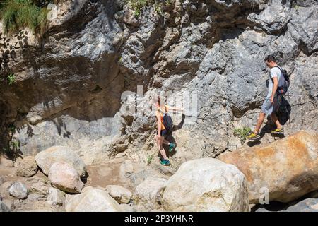 Two hikers, a man, and a woman walking one after another along an improvised path on a steep hillside holding a rope Stock Photo