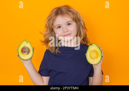 Kid hold red avocado in studio. Studio portrait of cute child with avocado isolated on yellow background, copy space Stock Photo