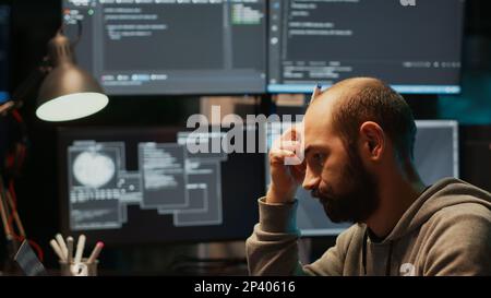 Thoughtful IT engineer brainstorming ideas in office, programming script and source code. Pensive man thinking about coding solution, developing app with html language late at night. Stock Photo