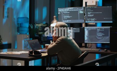 Young programmer answering phone call in office, talking on smartphone and coding user interface. Having remote conversation on mobile phone line, using html script on terminal window. Stock Photo