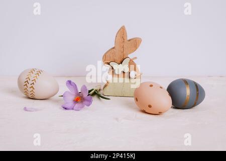 Wooden toy bunny, saffron flower and painted Easter eggs on white table. Easter holiday concept, closeup. Stock Photo