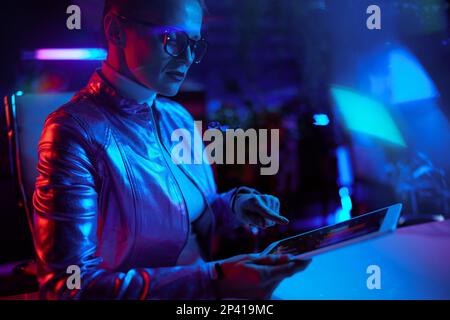 Neon metaverse futuristic concept. elegant middle aged woman in glasses using tablet PC in modern office. Stock Photo