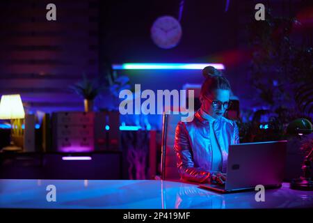 Neon metaverse futuristic concept. elegant business woman in glasses using laptop in modern office. Stock Photo