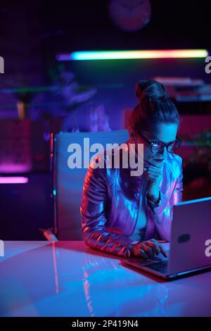 Neon metaverse futuristic concept. pensive elegant business woman in glasses using laptop in modern office. Stock Photo