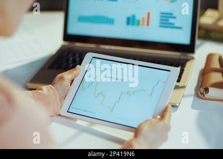 Seen from behind modern woman with laptop exploring charts, using tablet PC and checking trade exchange analysis chart and economy finance report in m Stock Photo