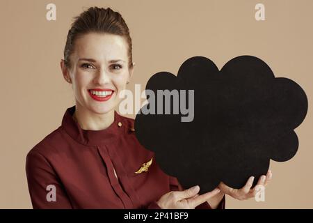 happy stylish stewardess woman against beige background with cloud shaped blackboard. Stock Photo