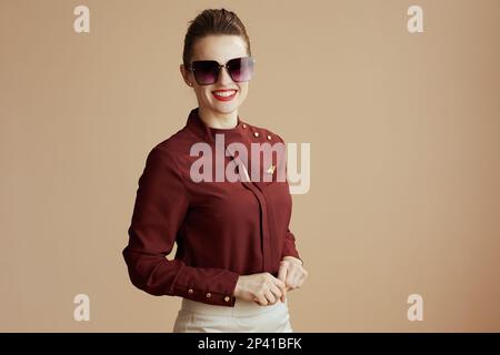 smiling stylish female stewardess against beige background with sunglasses. Stock Photo