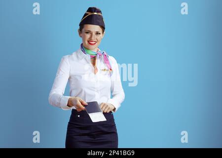 happy modern female stewardess against blue background in uniform with flight tickets and passport. Stock Photo