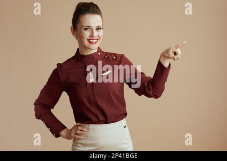 happy modern female flight attendant against beige background pointing at copy space. Stock Photo