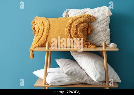 Stylish decorative pillows on shelving unit near blue wall Stock Photo