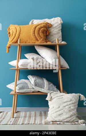 Stylish decorative pillows on shelving unit near blue wall Stock Photo