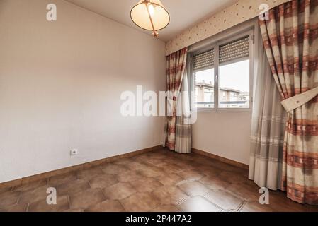 Empty room with dark brown stoneware floors, aluminum window with large curtains and lamp on the ceiling Stock Photo