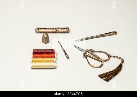 A set of old style copper scissors, thimbles and sewing accessories along with spools of multi colored thread on a plain white background Stock Photo