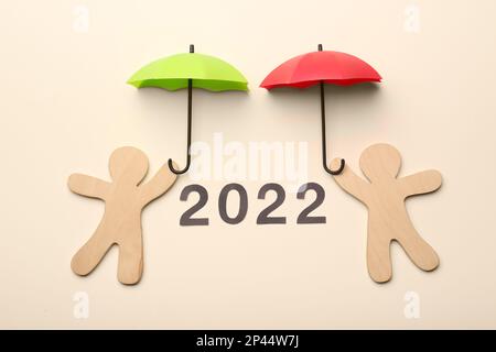 Mini umbrellas, figures of people and number 2022 on beige background, flat lay Stock Photo