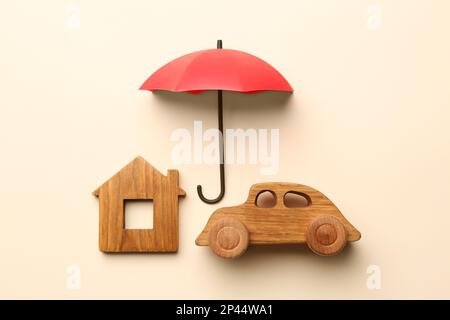 Mini umbrella, house model and toy car on beige background, flat lay Stock Photo