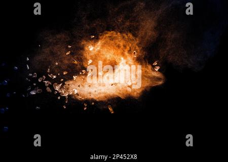 Split debris of stone exploding with orange dust against black background. Stock Photo