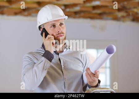 male architect talking on smartphone holding rolled up plans Stock Photo