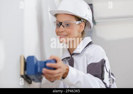 professional female builder using cordless sander on wall Stock Photo