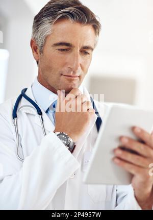 I wonder...a handsome mature male doctor holding a digital tablet while standing in a hospital corridor. Stock Photo