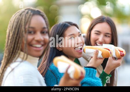 Asian woman eating hot dog with friends in a park Stock Photo