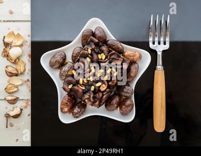 Piece of Homemade Toffee cake layer with cheesecake is decorated with sliced cashew nuts and dark chocolate covered almonds served with a fork on from Stock Photo