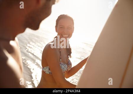 Love our relaxation time together. Portrait shot of a happy young woman smiling with her boyfriend and their surfboards at the beach. Stock Photo