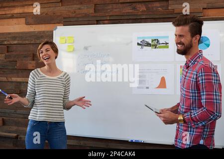 Theyve got their thinking caps on. two young designers brainstorming at a whiteboard. Stock Photo