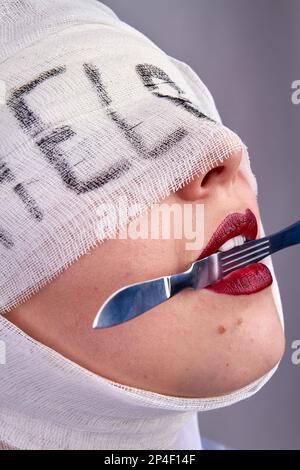 Close up womans face holding scalpel in her teeth. Bandaged head with help word. Stock Photo