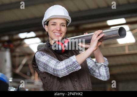 happy woman in dungarees carrying plastic pipes Stock Photo