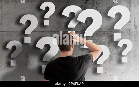 rear view of puzzled man scratching his head against concrete wall filled with question marks Stock Photo