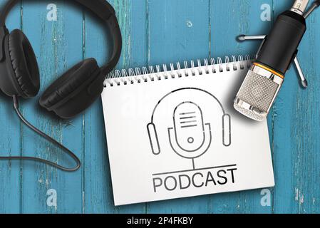 top view of headphones, microphone and note pad with PODCAST logo on rustic wooden table Stock Photo