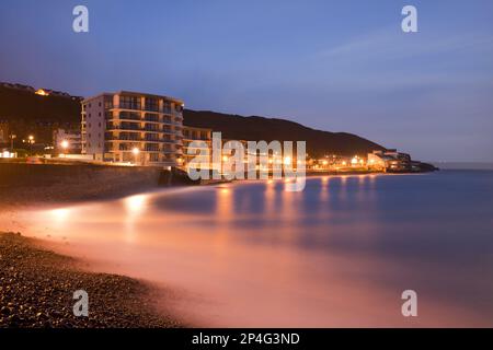 The sea rushes in over pebbles on the beach below the seafront promenade in front of sunrise, Westward Ho!, North Devon, England, United Kingdom Stock Photo