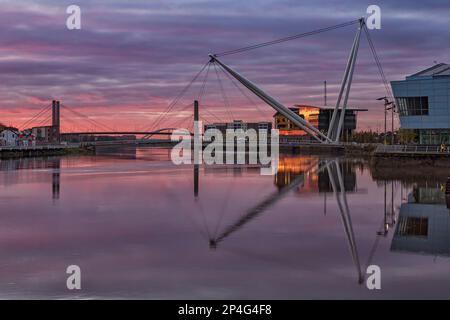 View of tidal river with footbridge and university building at sunrise, Newport City Footbridge, River Usk, Newport, South Wales, Wales Stock Photo