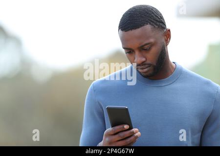 Sad black man reading chat on phone in the street Stock Photo